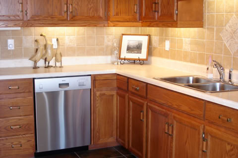 A kitchen with wooden cabinets, a stainless steel sink, a dishwasher, a countertop mixer, a microwave, and a gas stove.