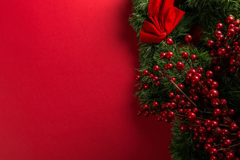 A Christmas wreath with red berries and a red bow on a red background.
