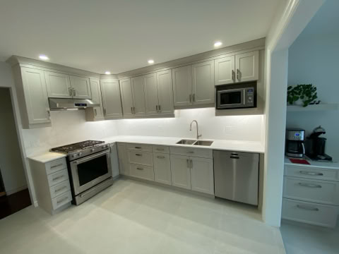 Modern kitchen with light gray cabinets, stainless steel appliances including a stove, microwave, and dishwasher, white countertops, and recessed lighting.