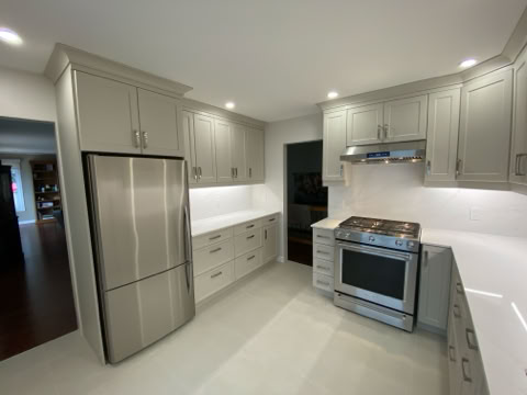 Modern kitchen with light gray cabinets, stainless steel refrigerator, and stove, white countertops, and recessed lighting.