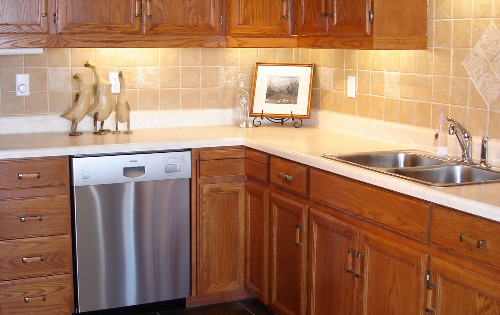 A kitchen with wooden cabinets, a stainless steel sink, a dishwasher, a countertop mixer, a microwave, and a gas stove.